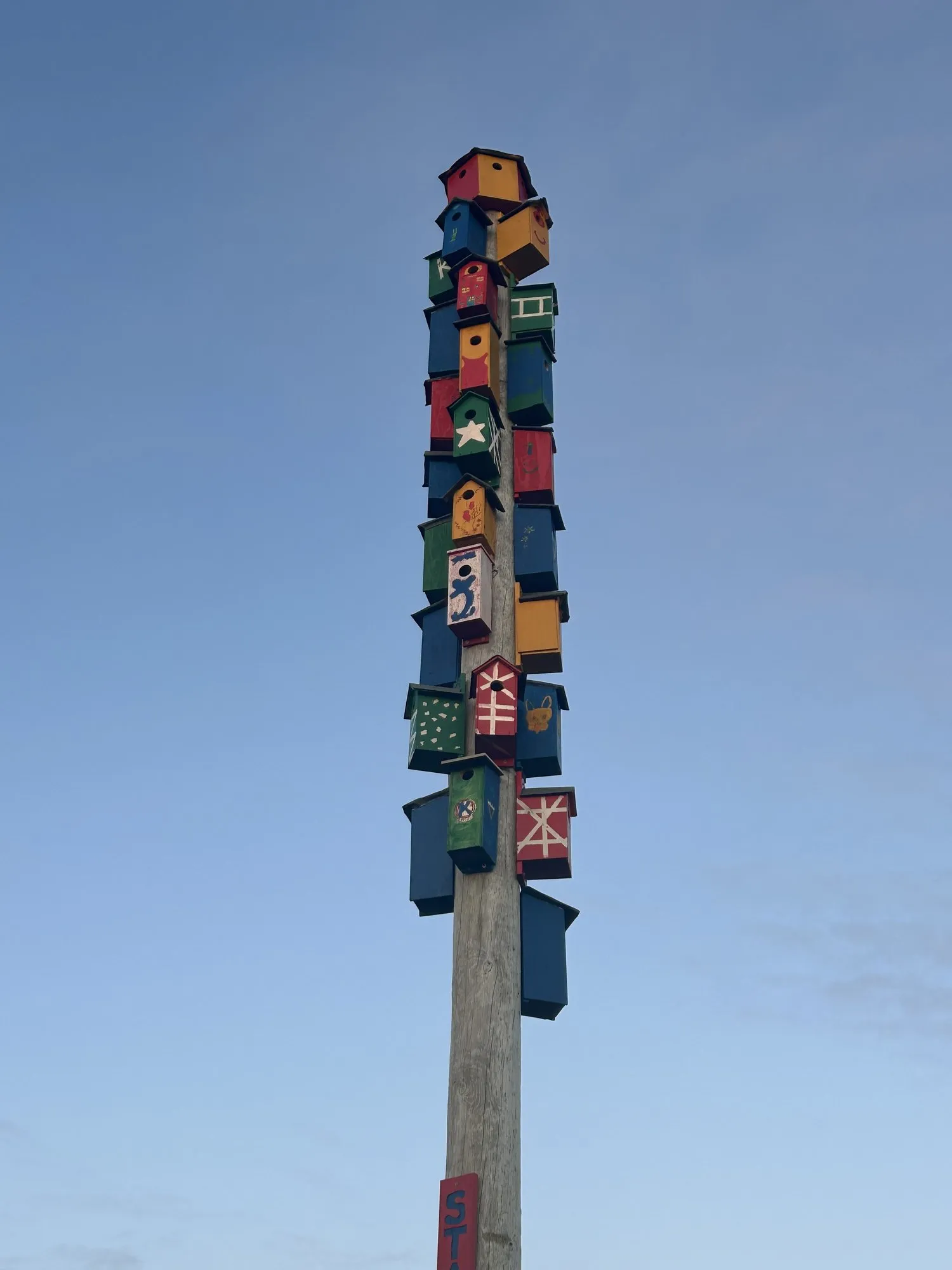 A tall pole stacked with colorful painted birdhouses against the sky.