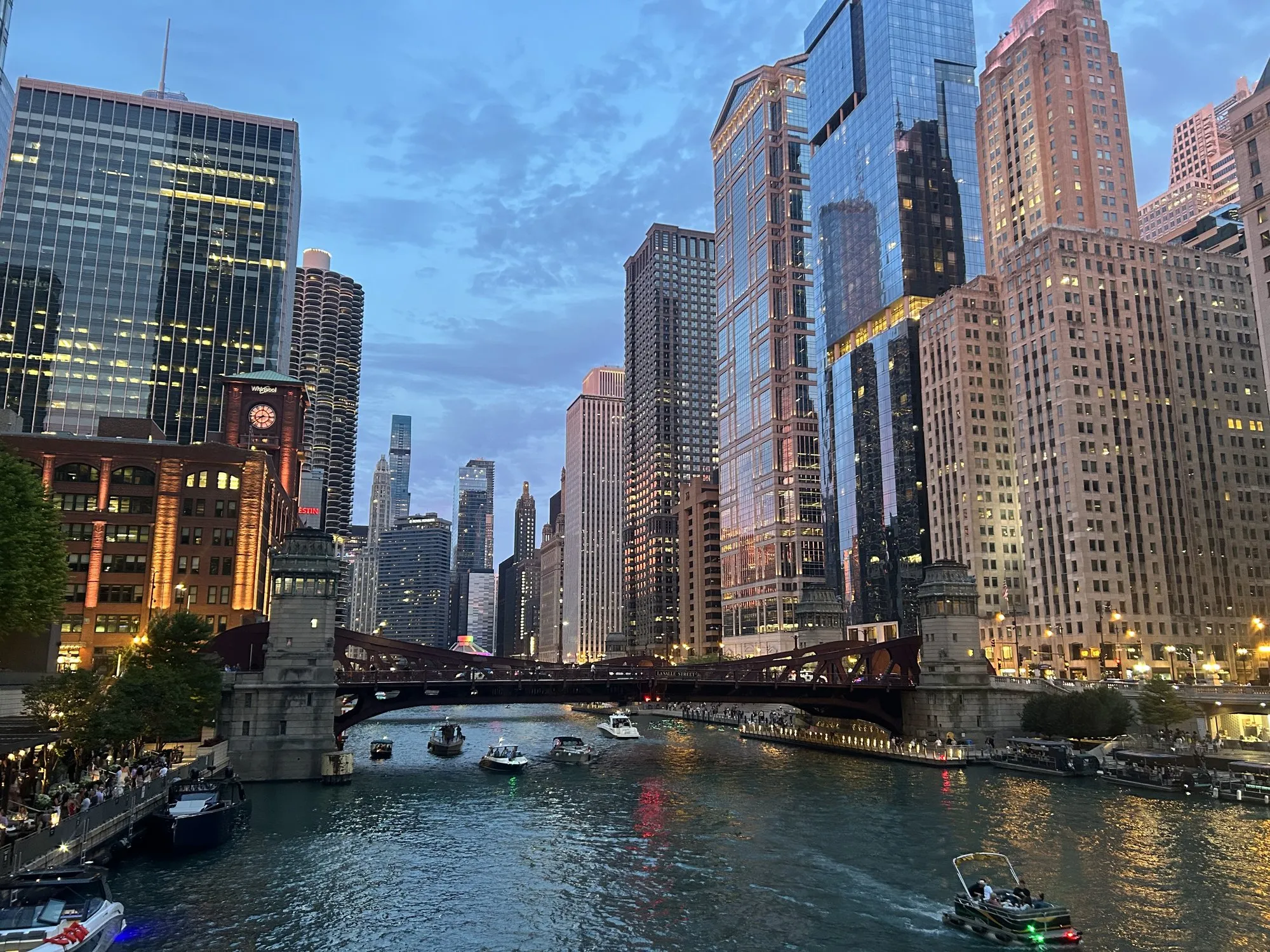 The Chicago River at dusk, lined with skyscrapers, boats on the water.