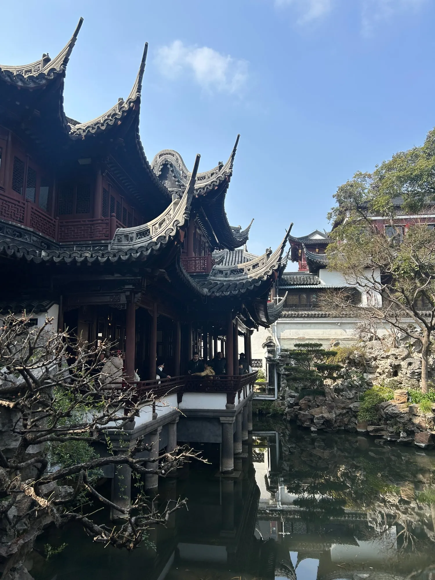 Dark tiled roofs with sharply upswept eaves over a pavilion, reflected in a still garden pond.