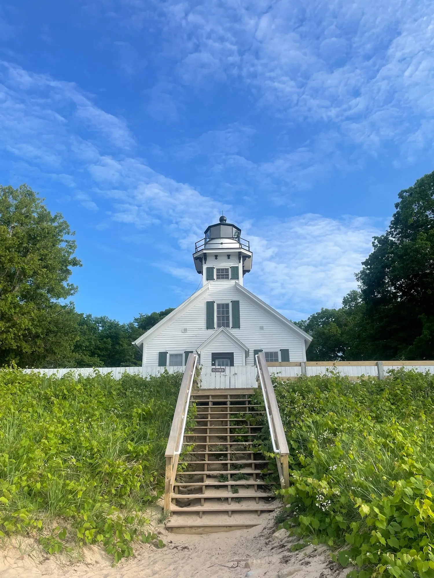 A white lighthouse at the top of wooden stairs through beach grass.