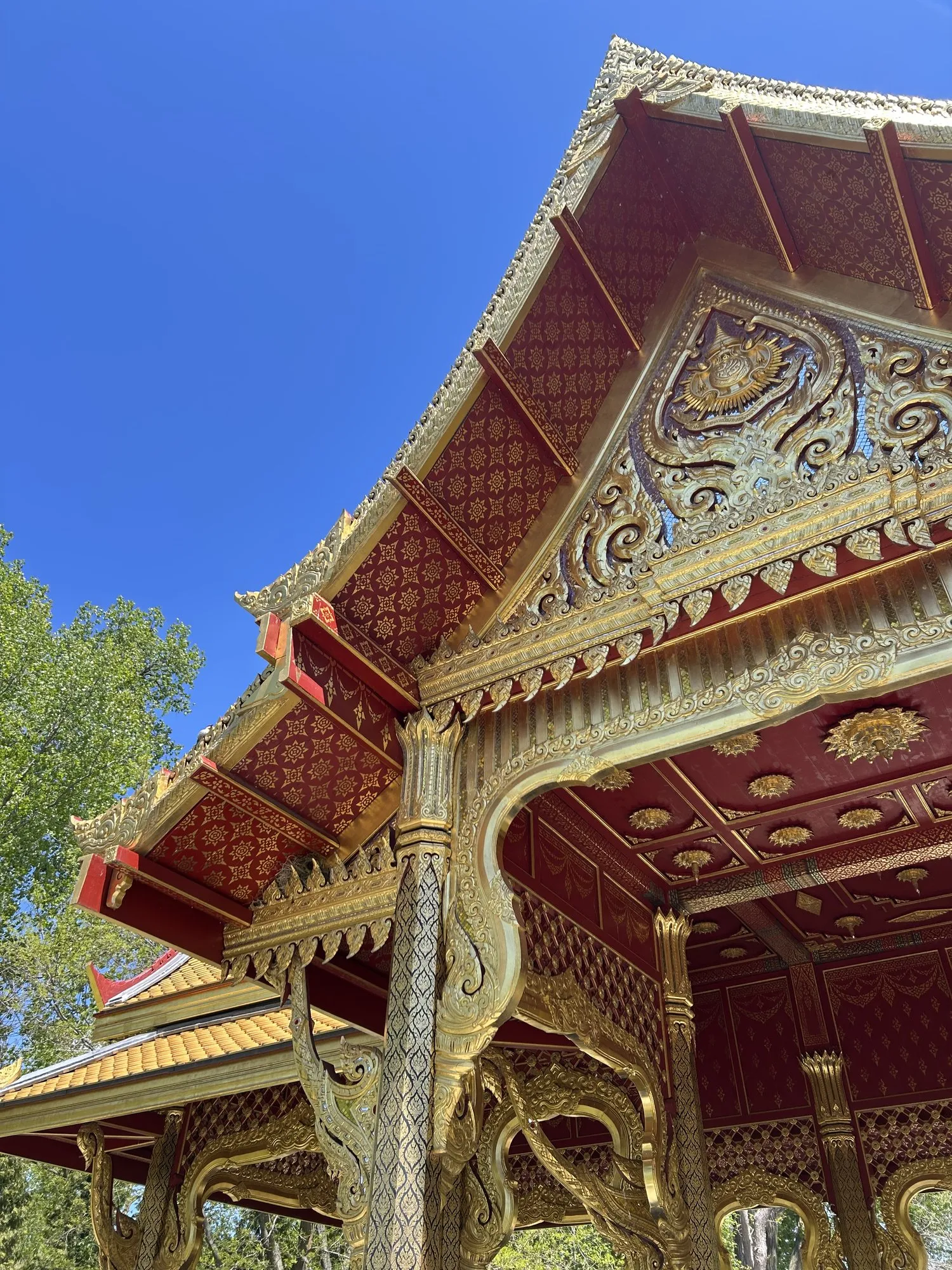 Looking up at an ornate red and gold temple roof against a blue sky.